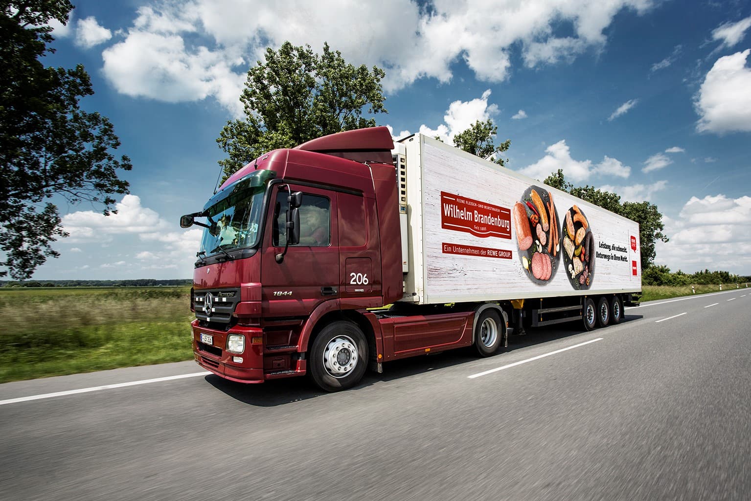 Wilhelm Brandenburg LKW mit Bild von Fleisch- und Wurstwaren, fährt auf einer Landstraße bei blauem Himmel