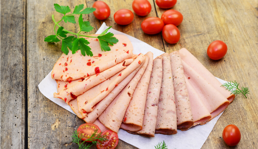 Verschiedene Sorten Aufschnitt, angerichtet auf Pergamentpapier mit frischen Kirschtomaten und Kräutern