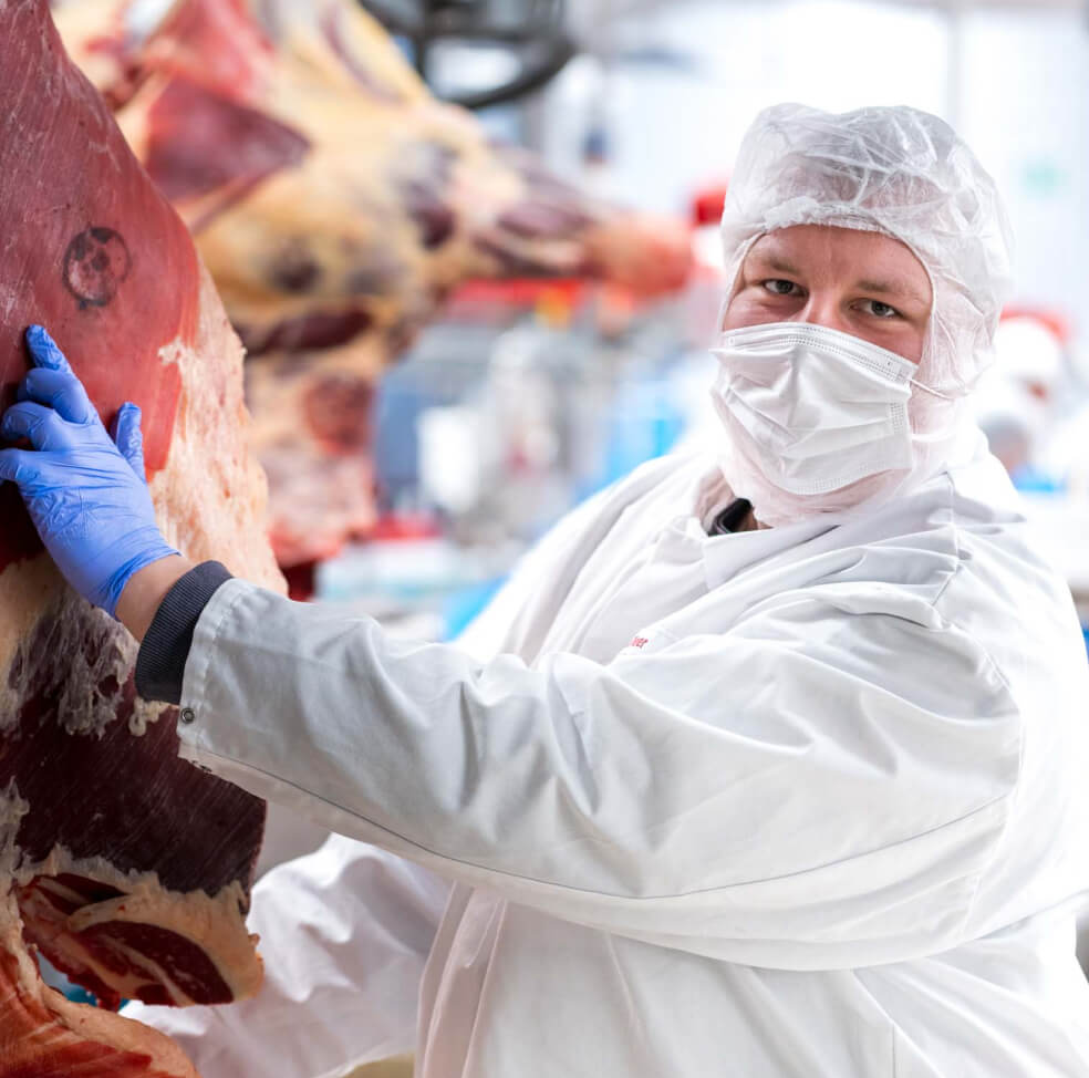 Mitarbeiter von Wilhelm Brandenburg in Schutzkleidung untersucht Fleischstück in der Produktion