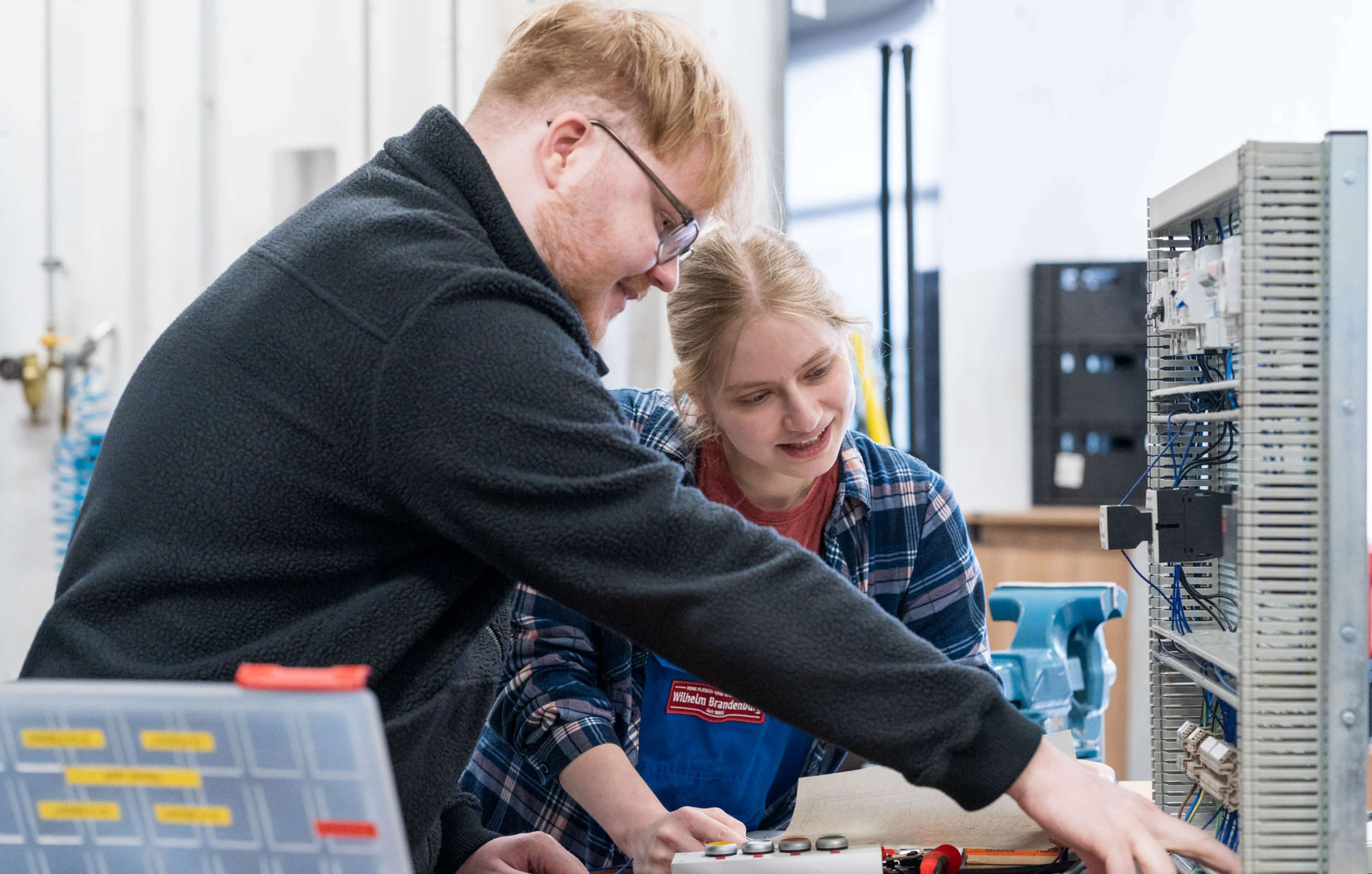 Zwei junge Techniker bei Wilhelm Brandenburg arbeiten gemeinsam an einem elektrischen Gerät