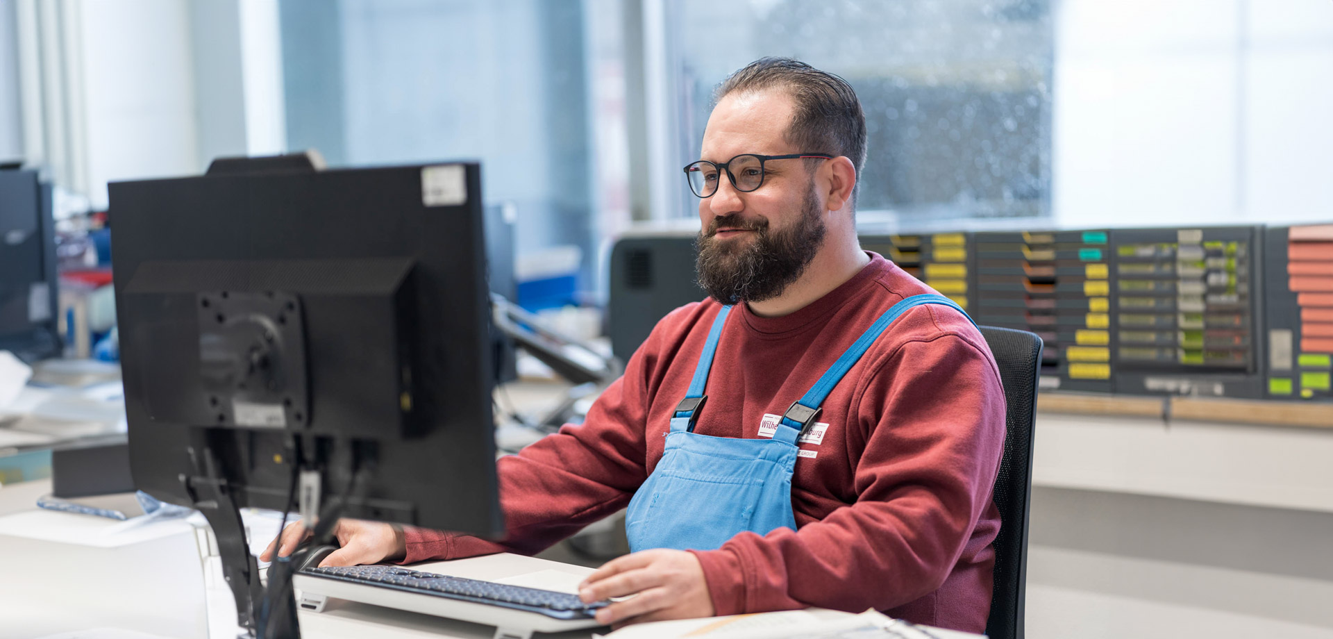 Mitarbeiter in blauer Schürze am Computer im Büro von Wilhelm Brandenburg