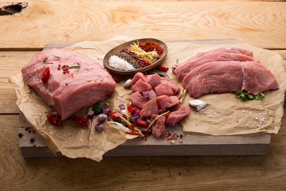 Frisches rohes Fleisch, in verschiedenen Schnitten angerichtet, zusammen mit Gewürzen auf einer Holzplatte