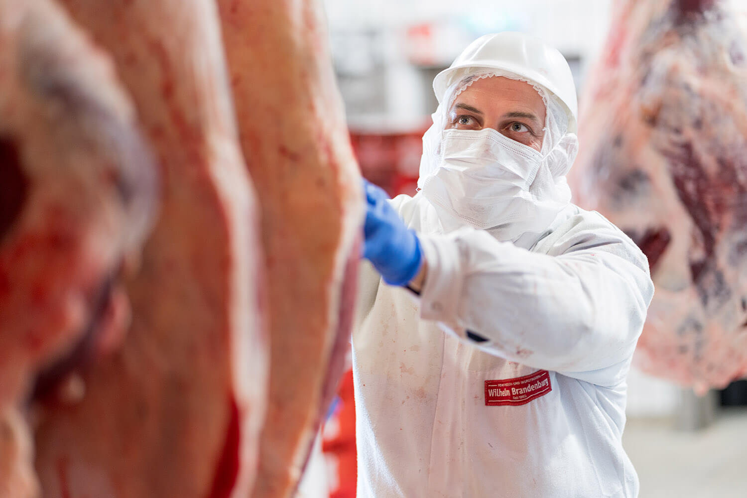 Mitarbeiter von Wilhelm Brandenburg in Schutzkleidung inspiziert Fleisch in einer Produktionshalle