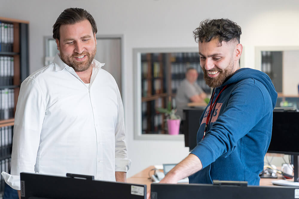 Zwei Kollegen bei Wilhelm Brandenburg arbeiten zusammen am Computer im Büro