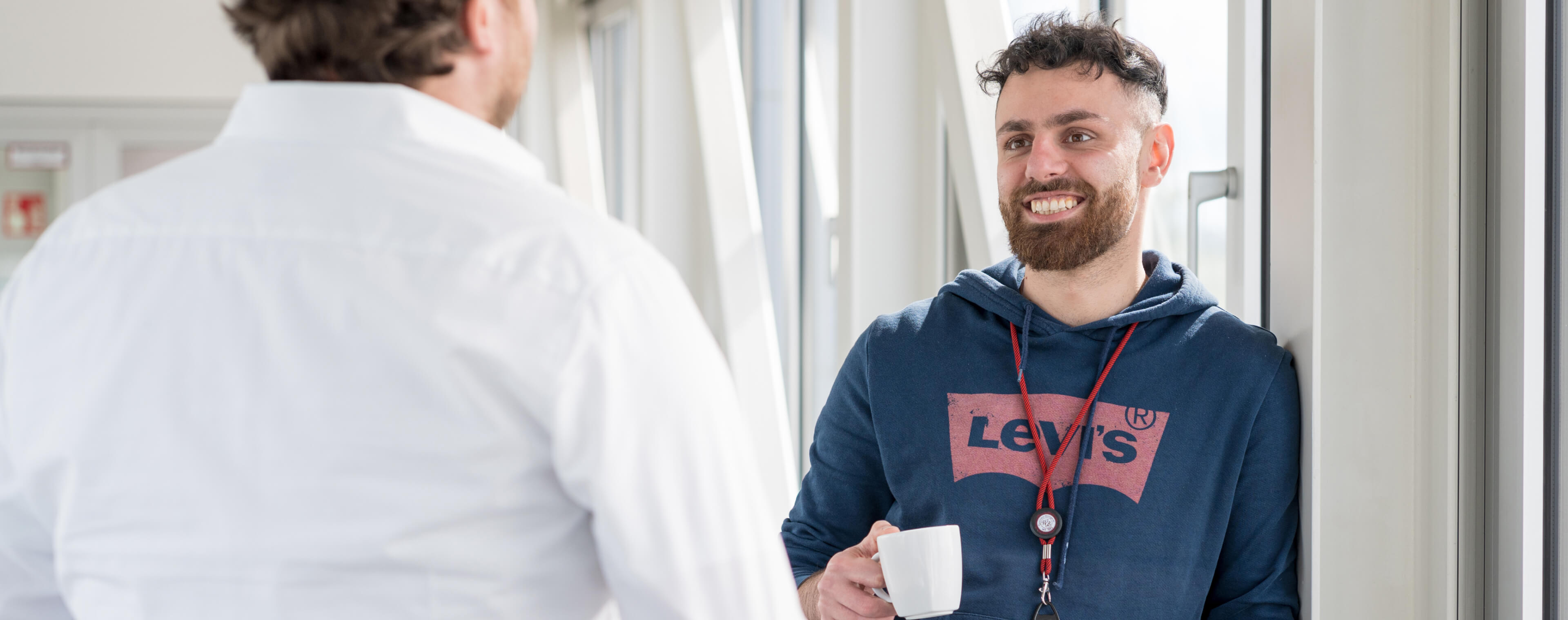 Zwei Männer im Gespräch, einer hält eine Tasse in der Hand, während er lächelt