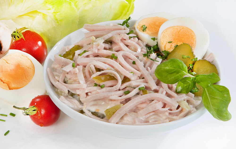 Wurstsalat mit Gewürzgurken, Zwiebeln, hartgekochten Eiern, Tomaten und Salatblättern, serviert in einer Schale